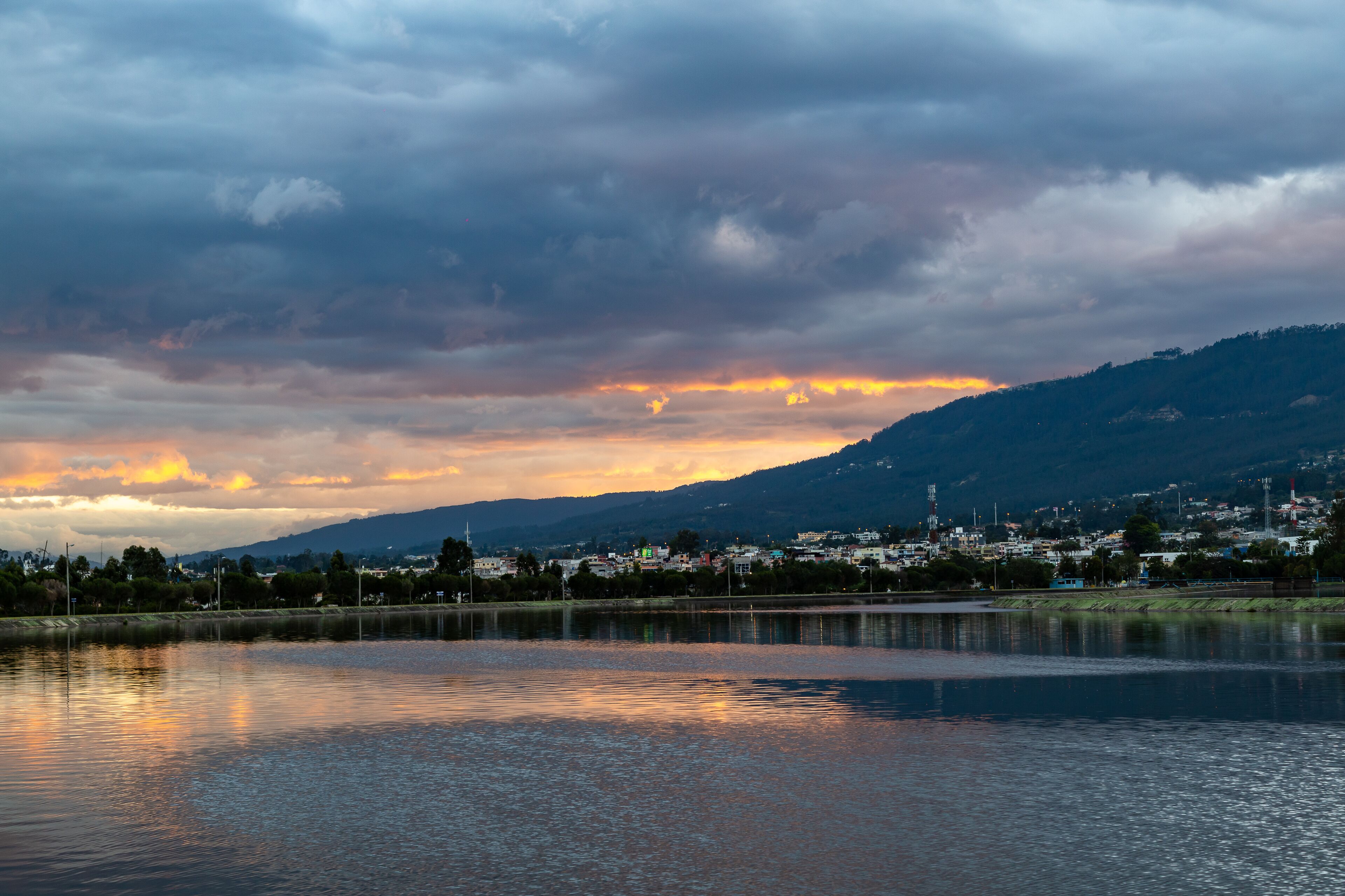 A lake with a city in the background, a cloudy sky, and a sunset.