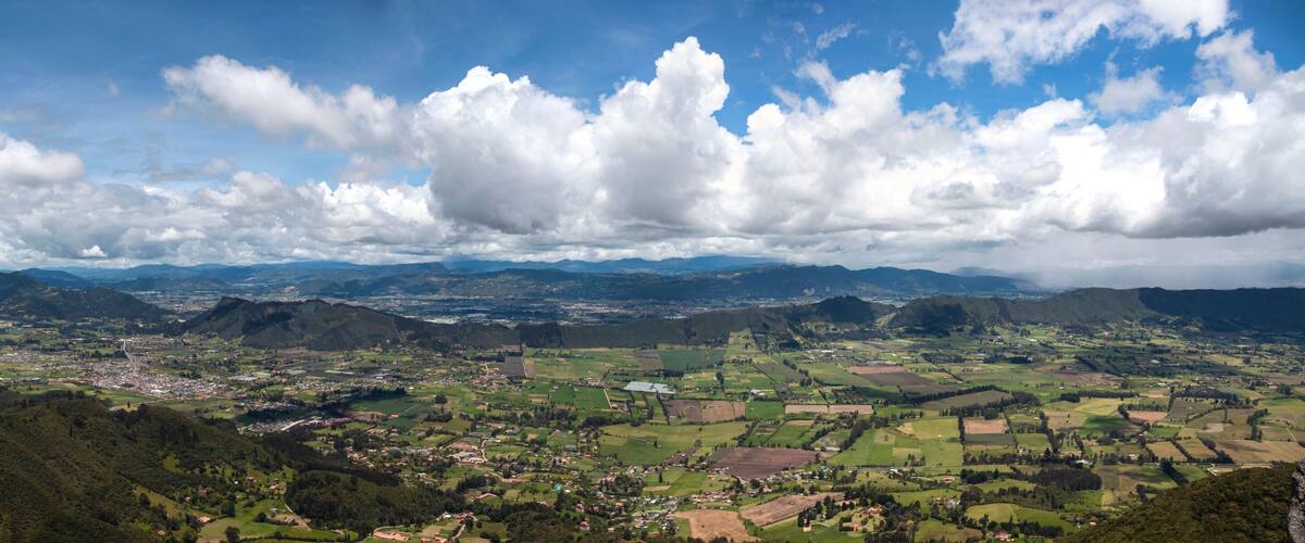A panoramic view of a valley with mountains, a town, and scattered fields.