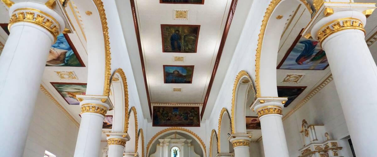An ornate church interior with white columns, gold accents, and religious paintings on the ceiling.