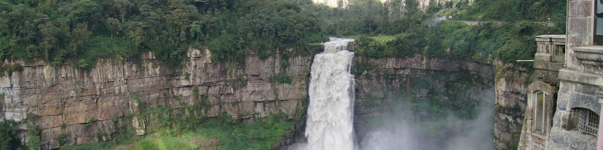 Uma cascata despencando por um penhasco íngreme, cercada por vegetação exuberante e uma construção de pedra.