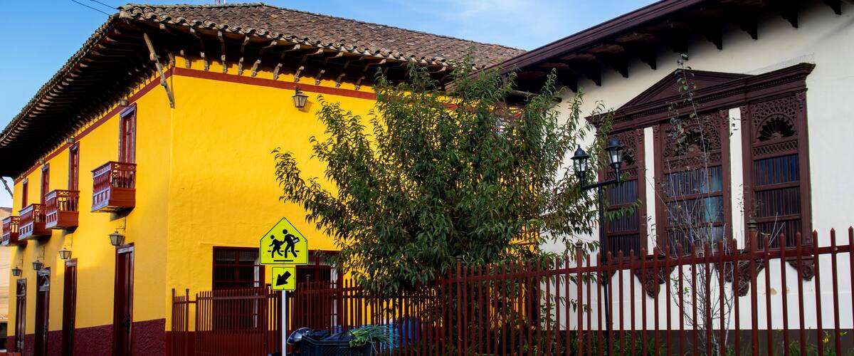 A yellow building with a red fence, a motorcycle, and a pedestrian crossing sign.