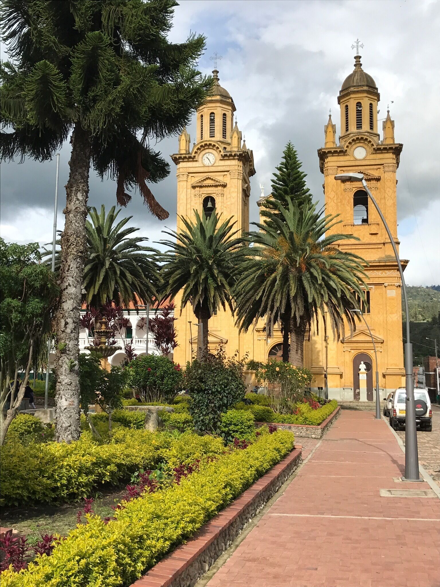 A historic church with two bell towers, surrounded by well-maintained gardens and palm trees.