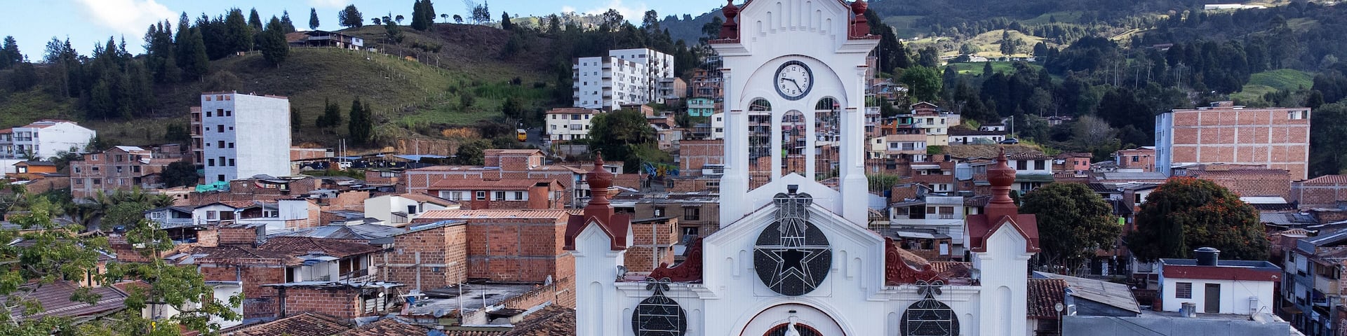 A white church with a clock tower, surrounded by a densely packed urban area with red-tiled roofs.