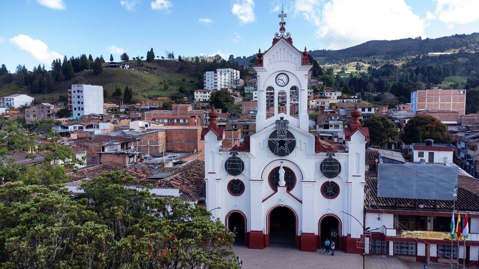 A white church with a clock tower, surrounded by a densely packed urban area with red-tiled roofs.