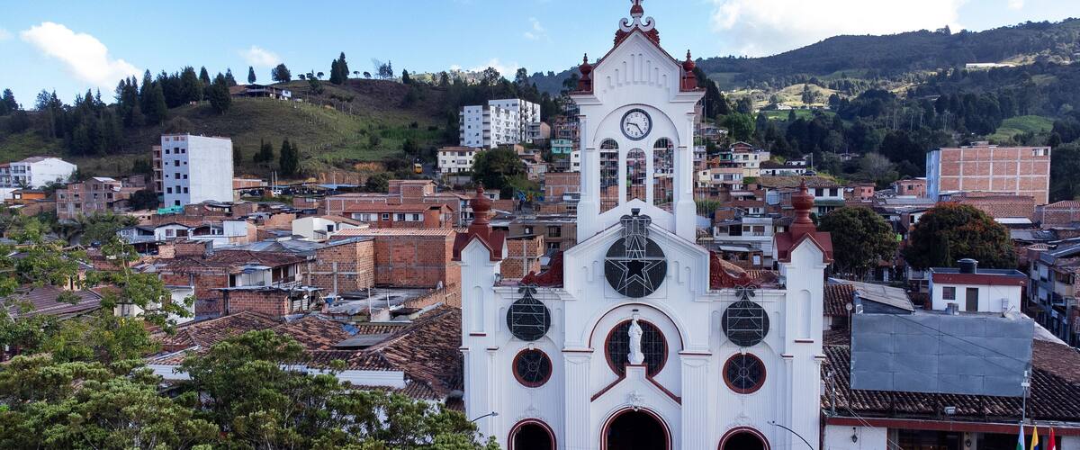 A white church with a clock tower, surrounded by a densely packed urban area with red-tiled roofs.