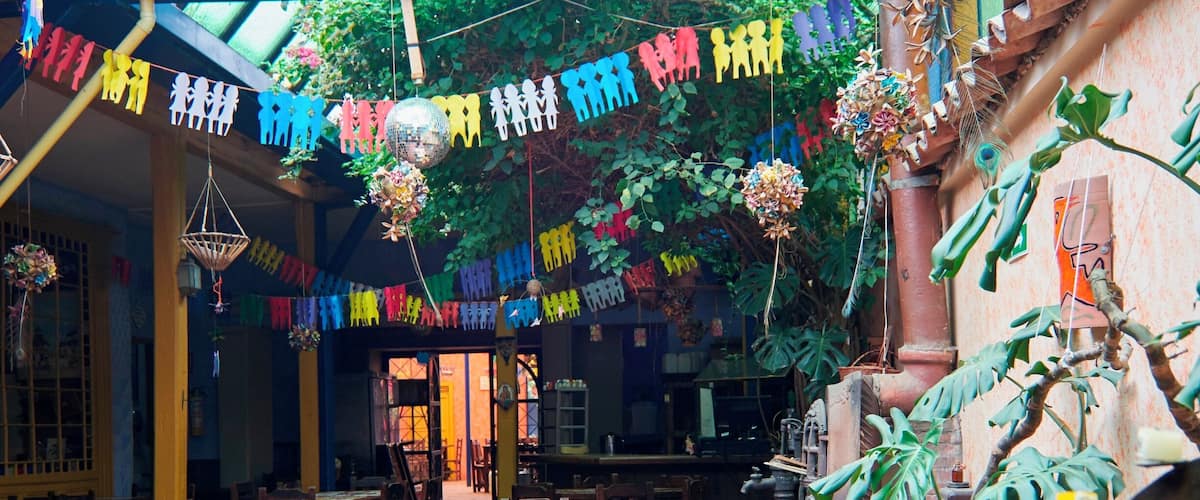 A restaurant with wooden tables and chairs, colorful decorations, and hanging plants.