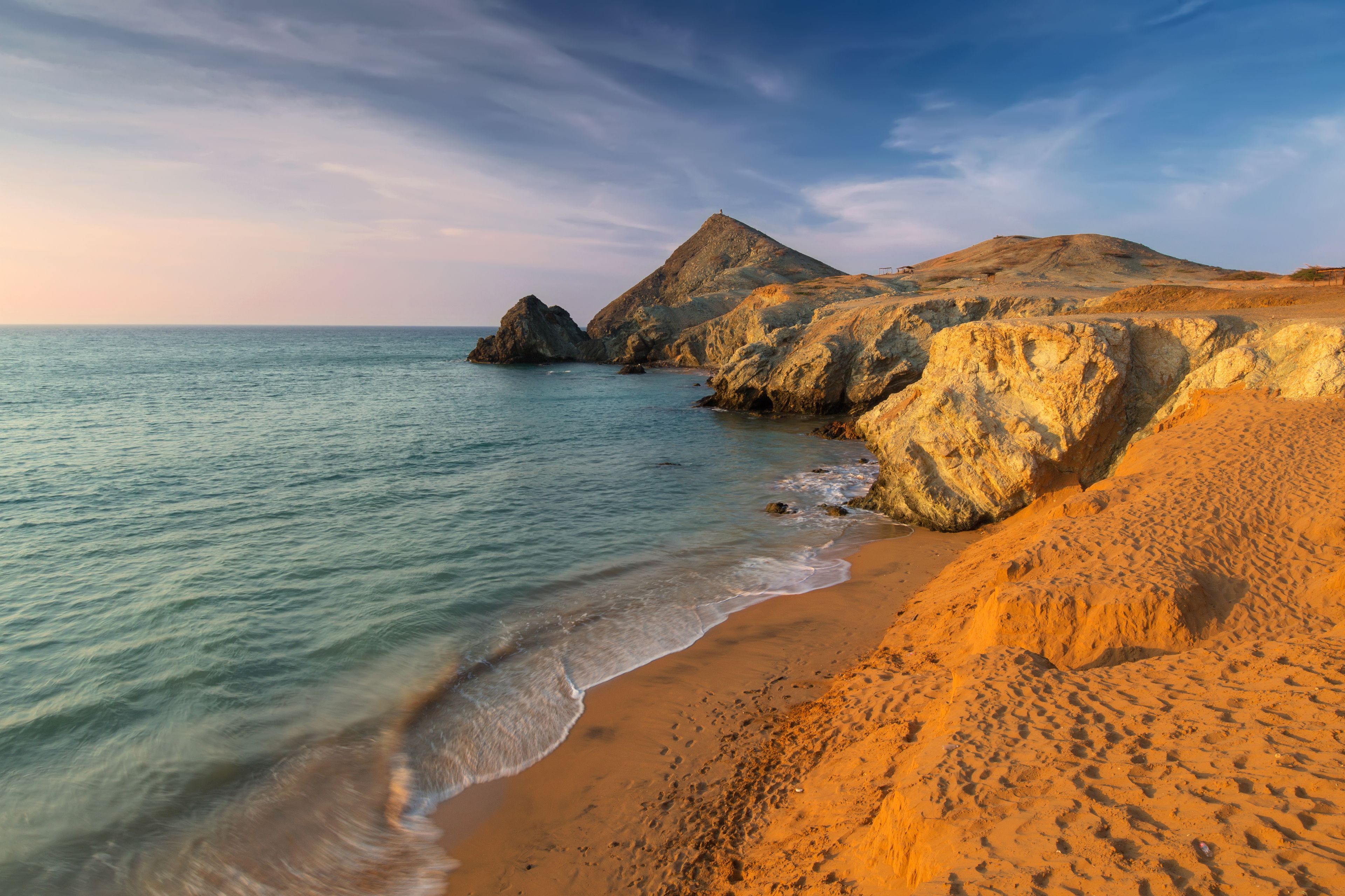 Un paisaje costero con playa arenosa, mar tranquilo y acantilados rocosos.