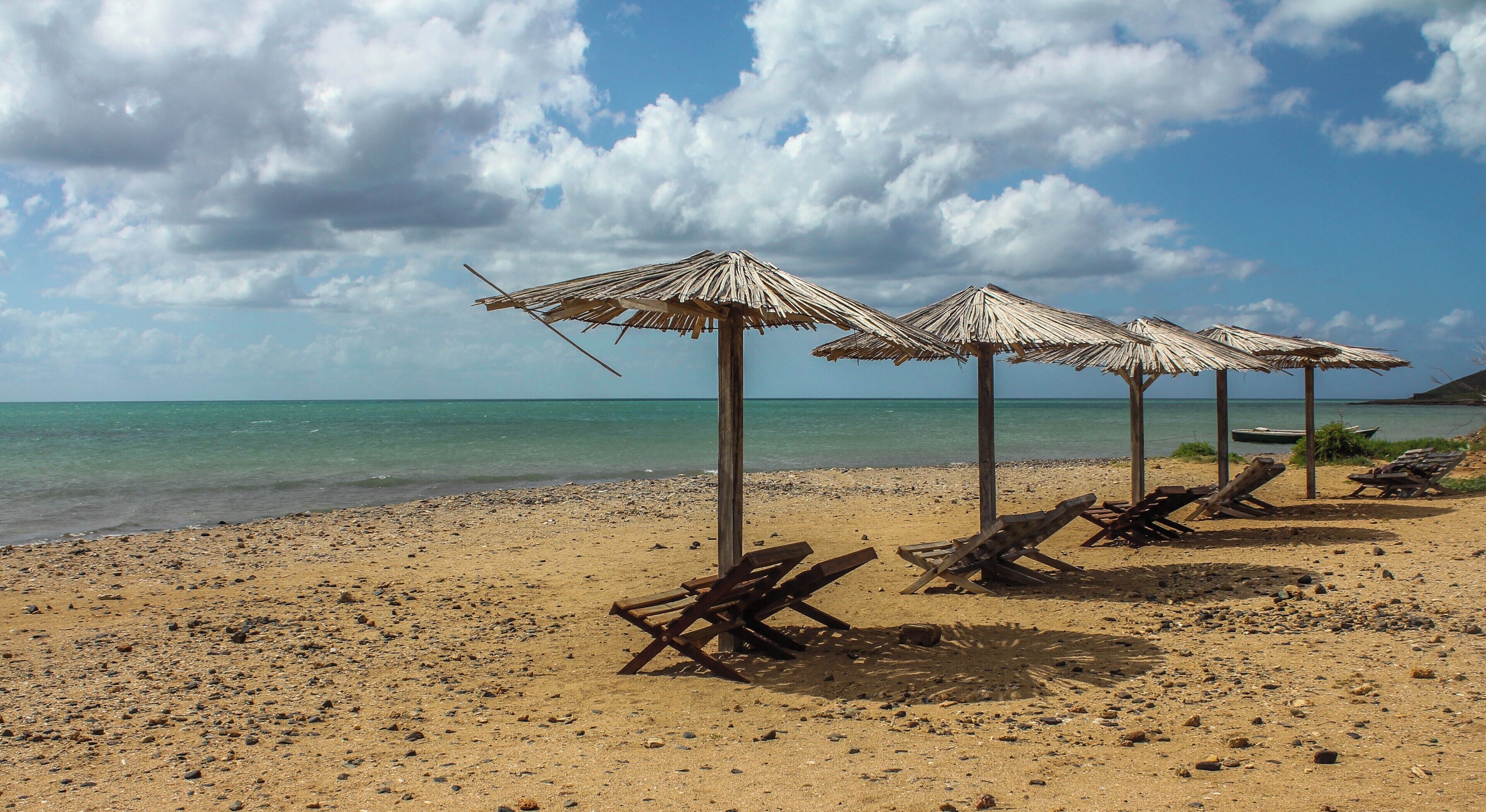 A beach with thatched umbrellas and wooden lounge chairs.