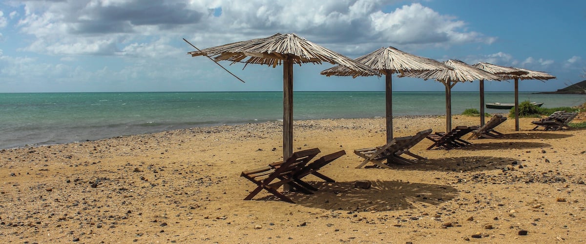 A beach with thatched umbrellas and wooden lounge chairs.