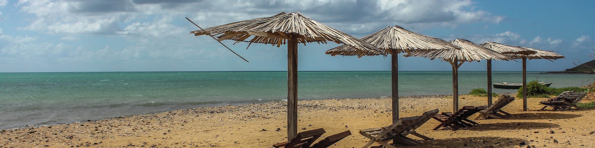 A beach with thatched umbrellas and wooden lounge chairs.