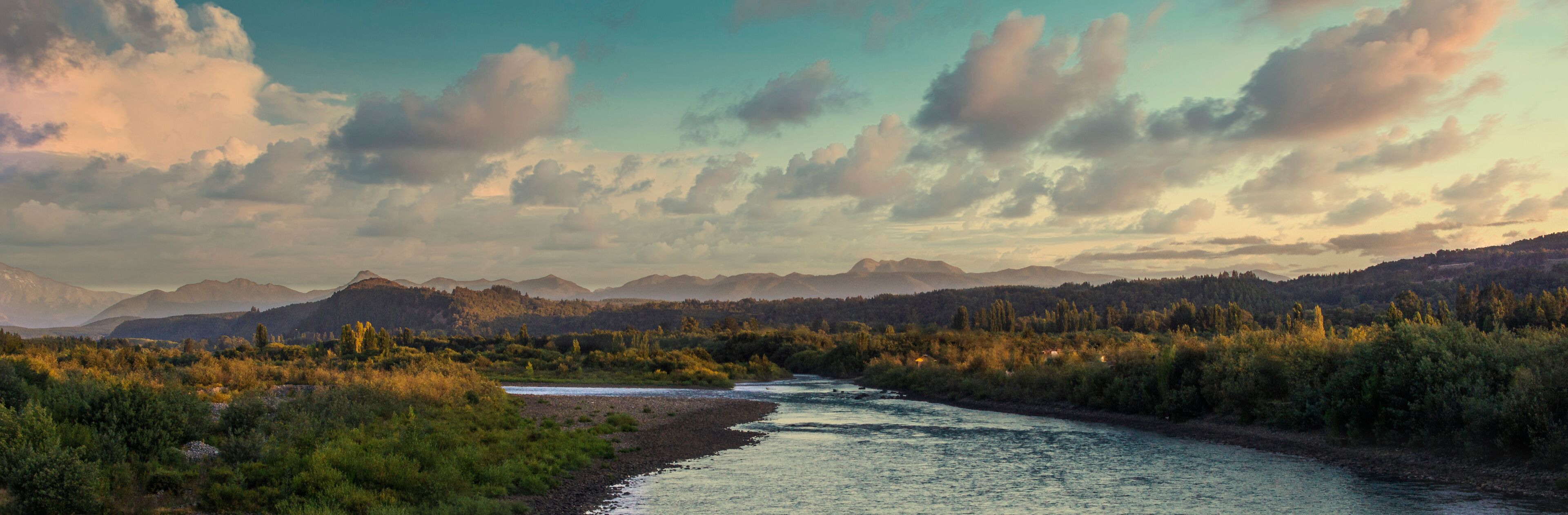 A river flowing through a forested valley with mountains in the background.