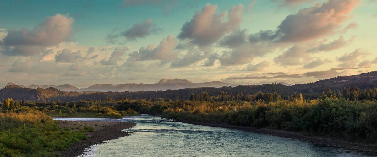 A river flowing through a forested valley with mountains in the background.