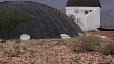 A dome structure with a white building in the foreground and mountains in the background.