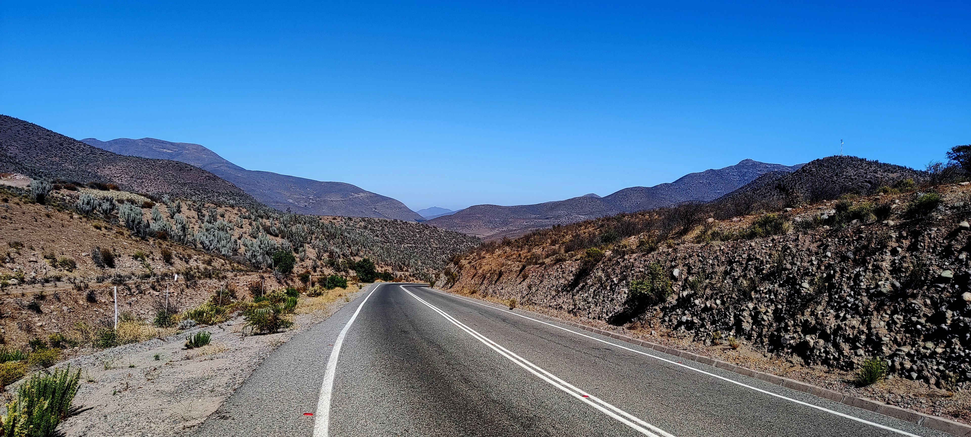 A two-lane road in a desert landscape with mountains in the background.