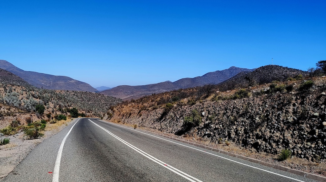 A two-lane road in a desert landscape with mountains in the background.
