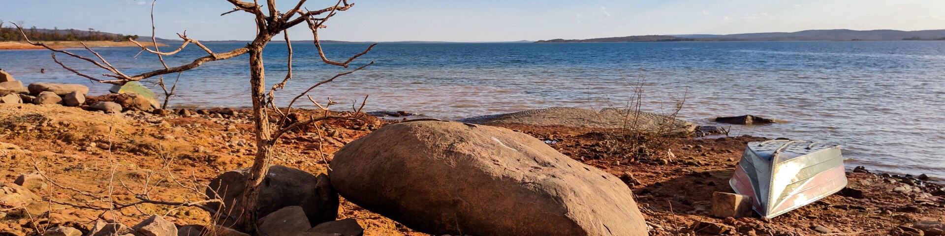 Linda vista da marchem da represa de três marias, com água límpida, céu azul com nuvens e uma lancha logo a frente de grande pedra, na região de Três Marias, Minas Gerais, Brasil.