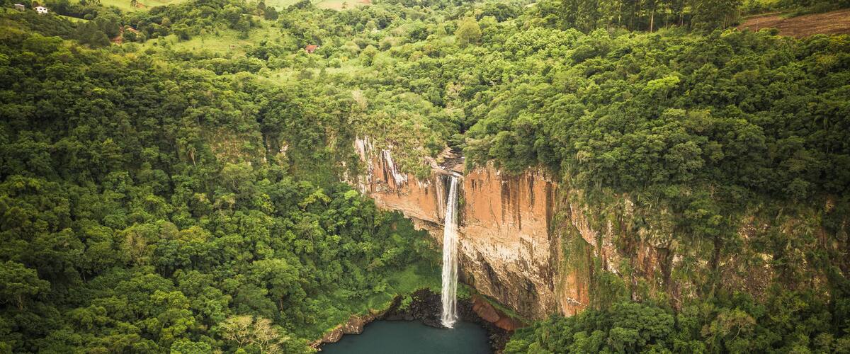 A waterfall cascading into a river surrounded by dense forest and hills.