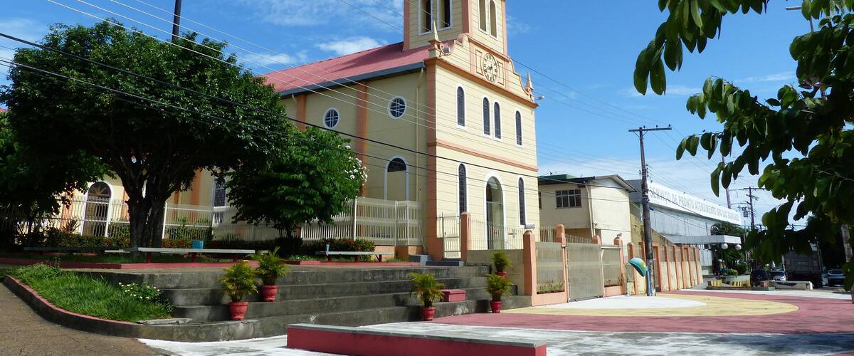 A church with a bell tower, surrounded by trees and a paved area with benches.