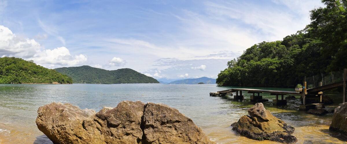 A beach with clear water, rocky outcrops, and lush green hills in the background.
