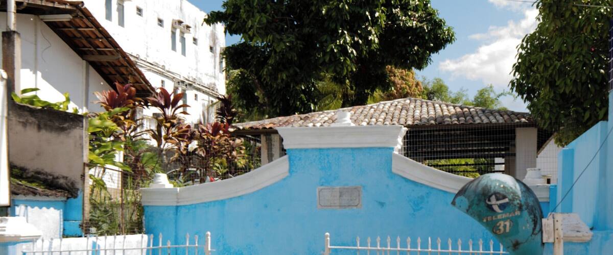 A blue building with a white gate, a tiled roof, and a tree in the background.