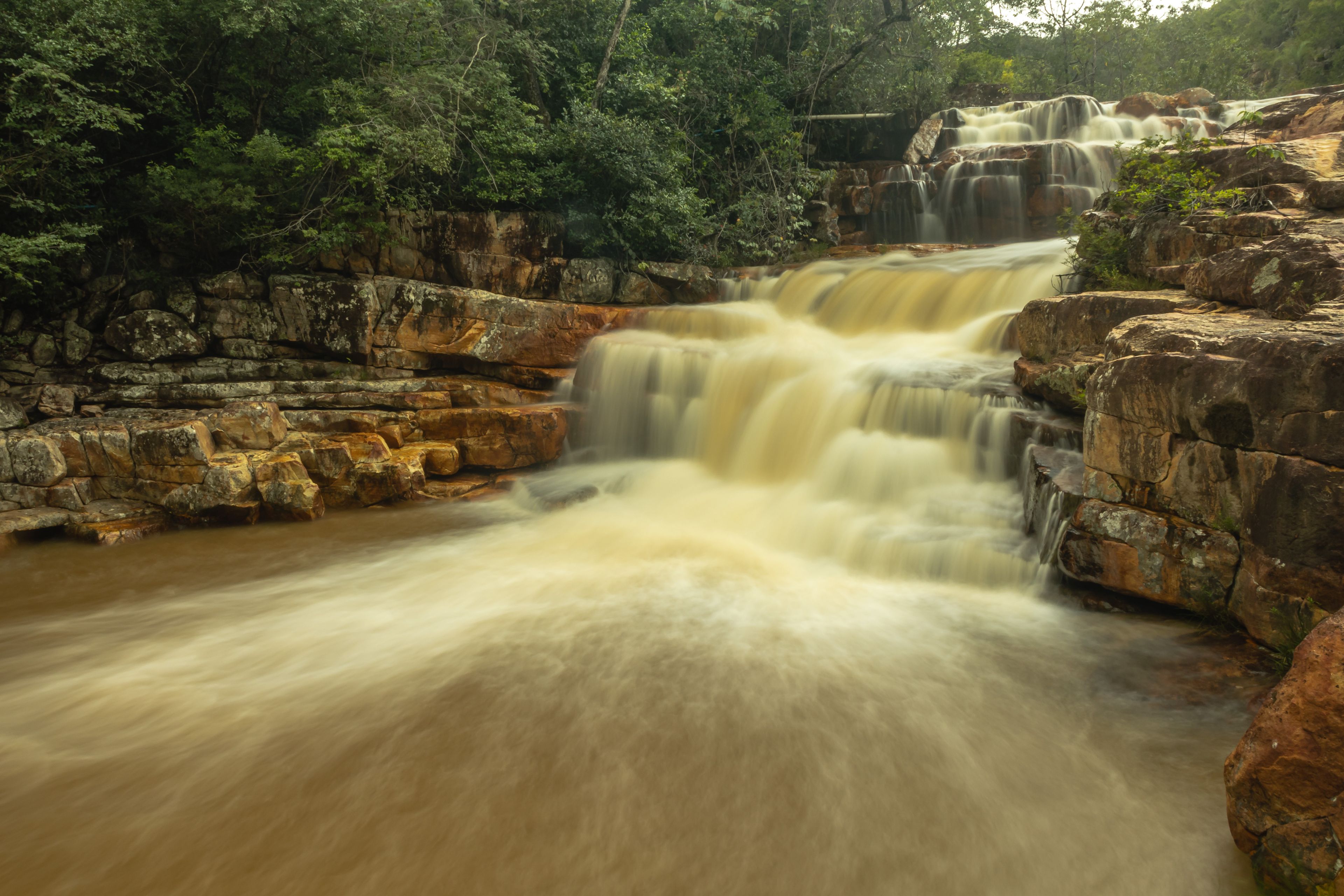 Uma cascata em vários níveis, rodeada por terreno rochoso e vegetação densa.