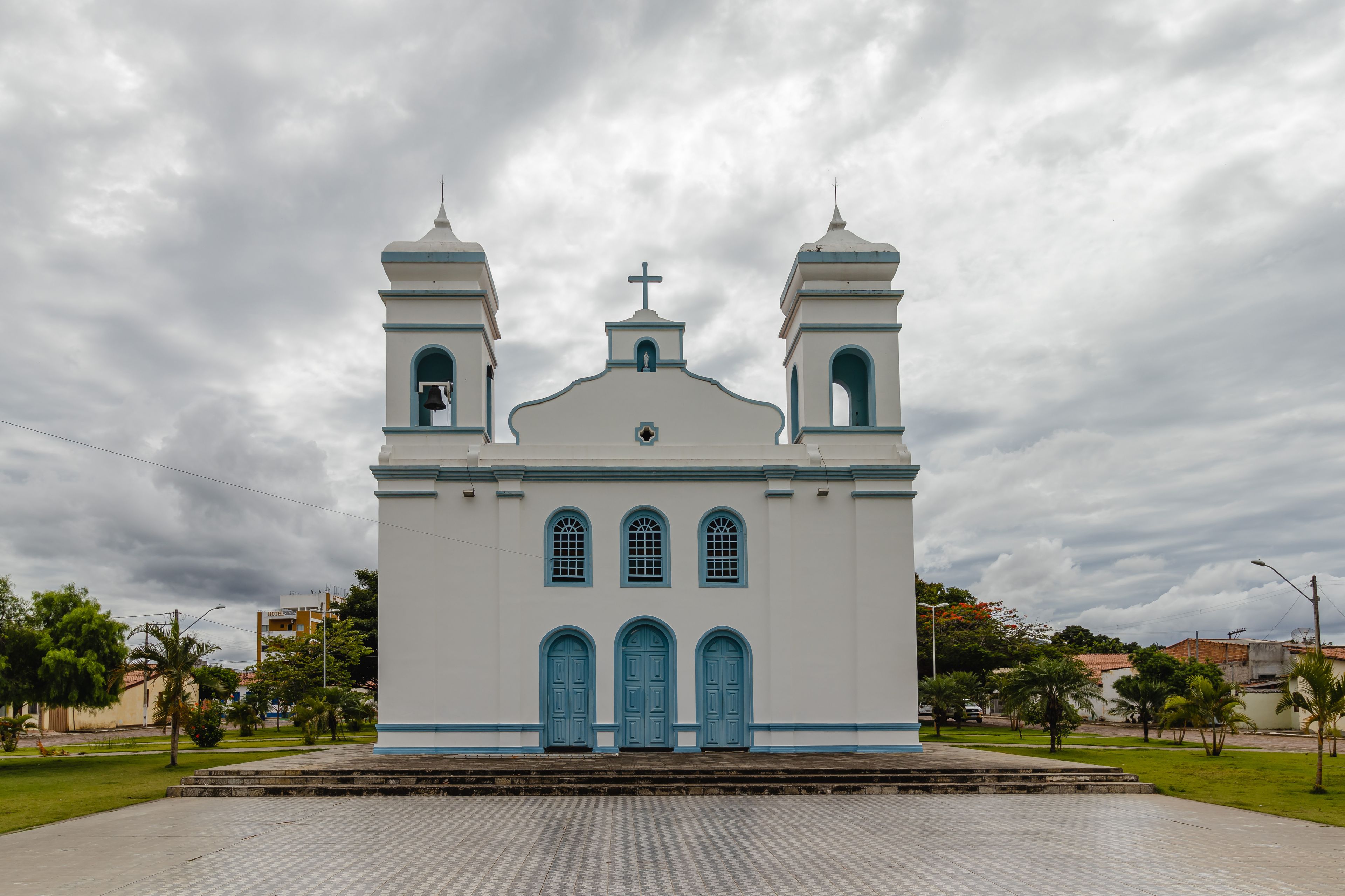 A white church with blue doors and windows, two bell towers, and a cross on the roof.