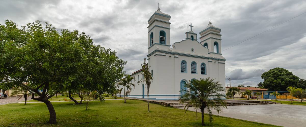 A white church with blue trim and two towers, surrounded by green grass and trees.