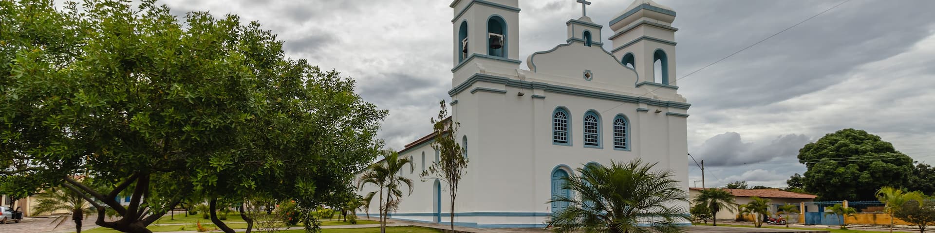 A white church with blue trim and two towers, surrounded by green grass and trees.