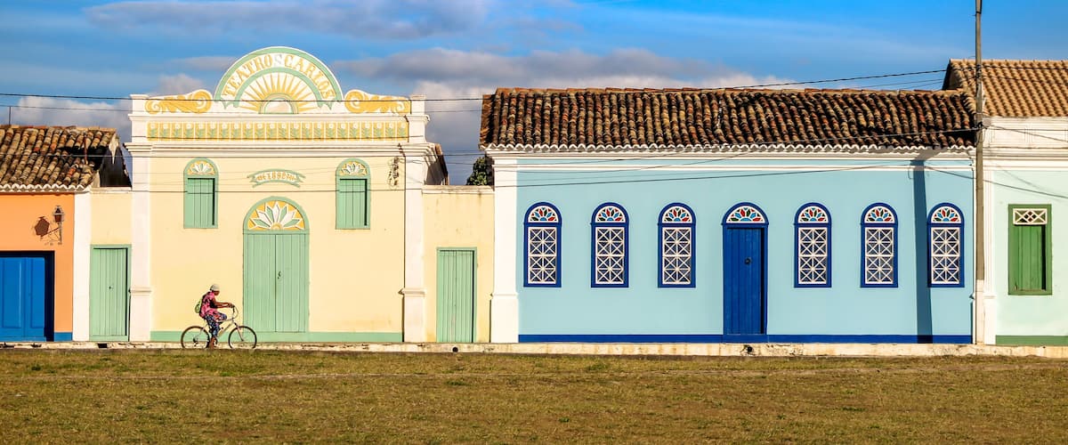 A row of colorful buildings with green doors and windows, a cyclist, and a clear sky.