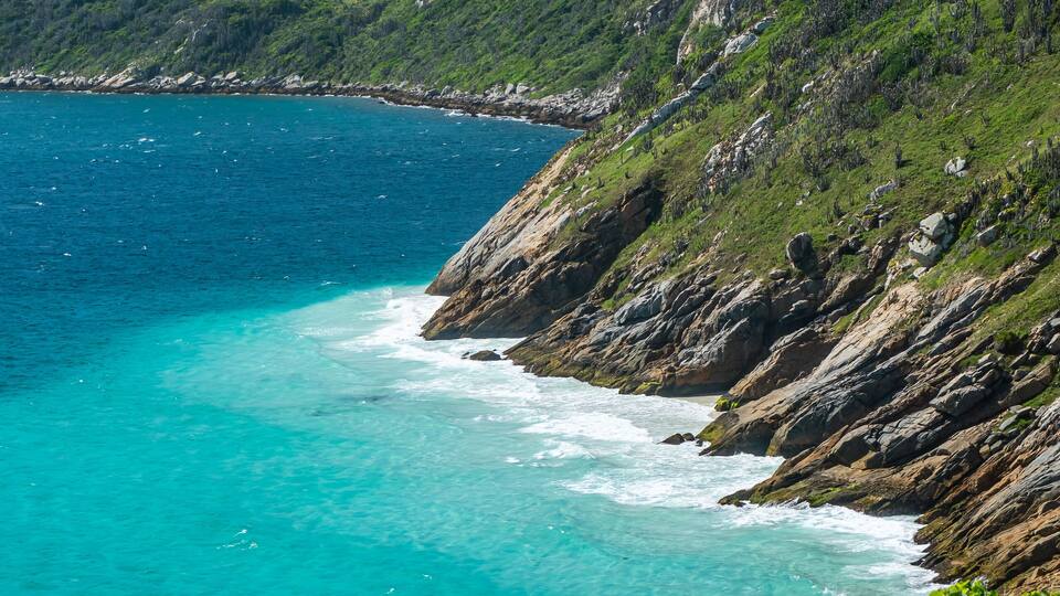 A coastal landscape with turquoise waters, green hills, and rocky cliffs.