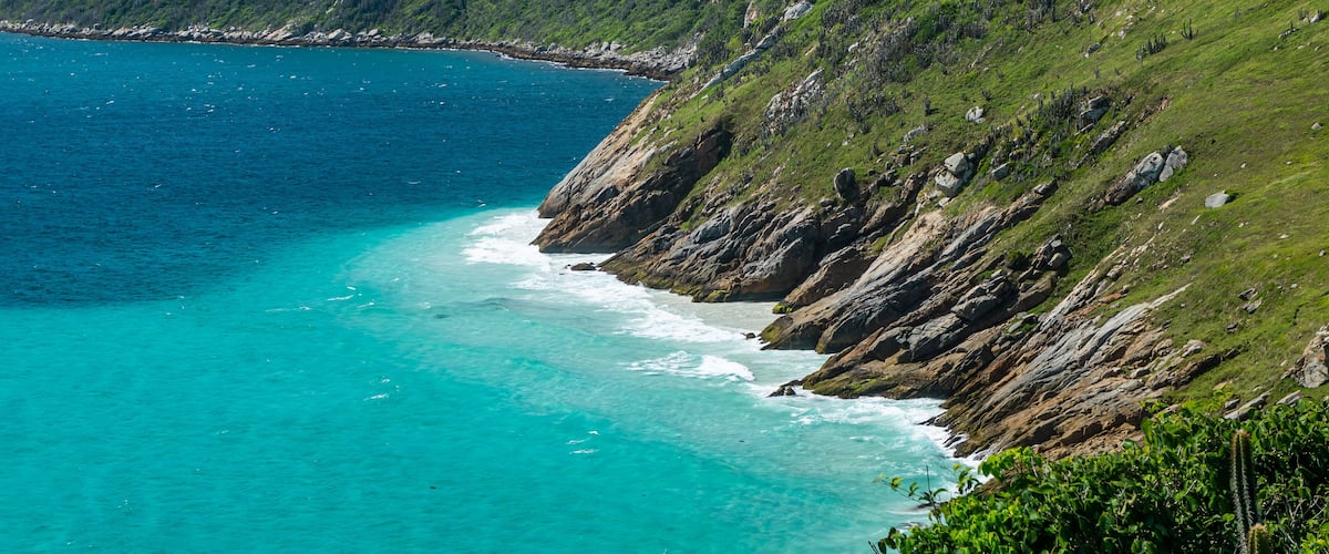 A coastal landscape with clear turquoise waters, rocky cliffs, and lush green hills.