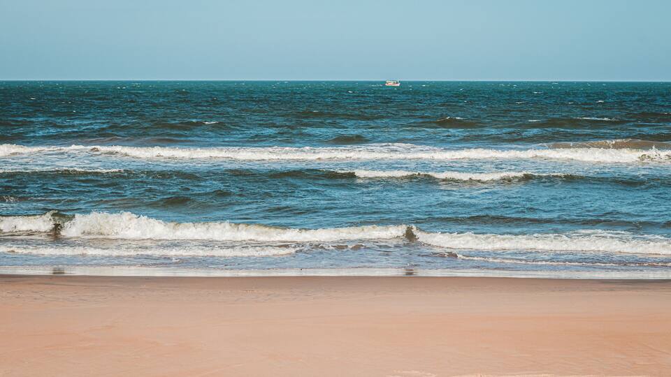 A beach with waves and a boat in the distance.