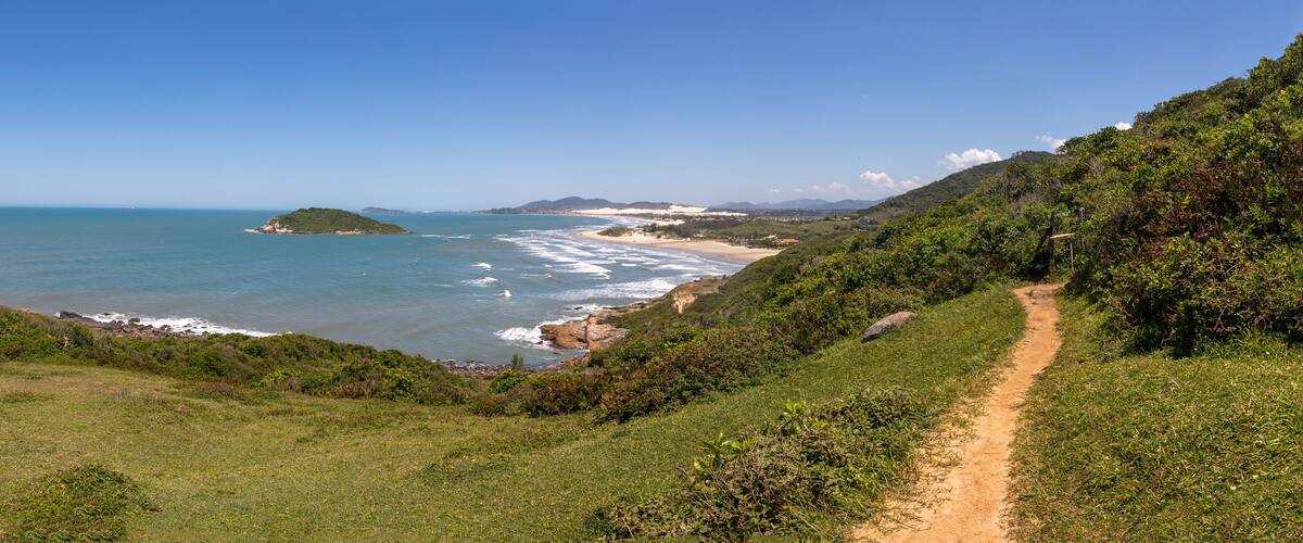 A coastal landscape with a dirt path, grassy hills, and a beach.