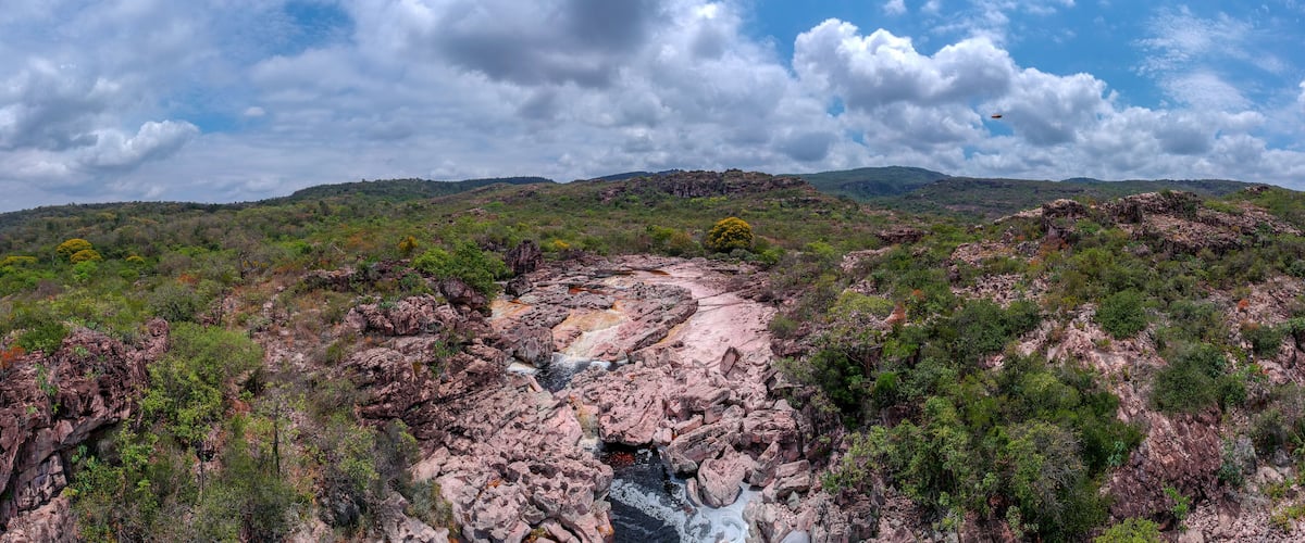 A rocky landscape with a waterfall, green vegetation, and distant hills under a partly cloudy sky.