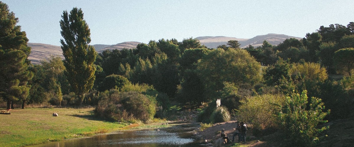 A calm river with a grassy bank, trees, and a distant mountain range.