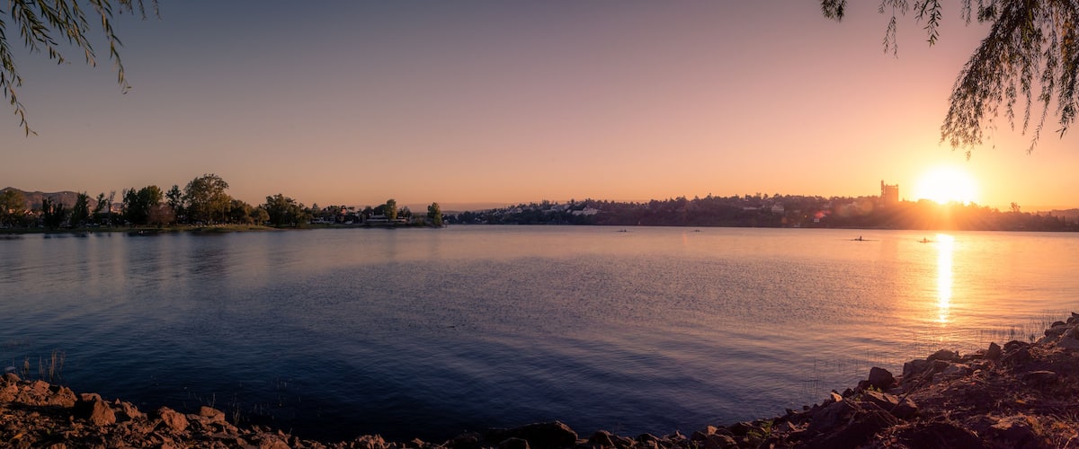 Un lac paisible au coucher du soleil, avec la silhouette d’une ville en arrière-plan.