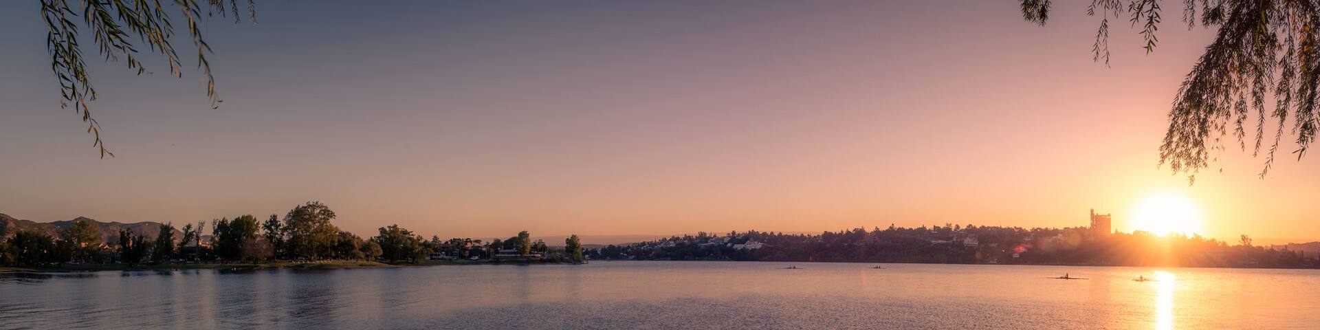A calm lake at sunset with a city skyline in the background.