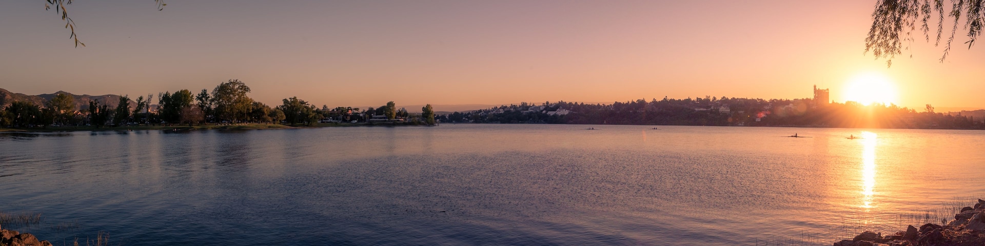 A calm lake at sunset with a city skyline in the background.