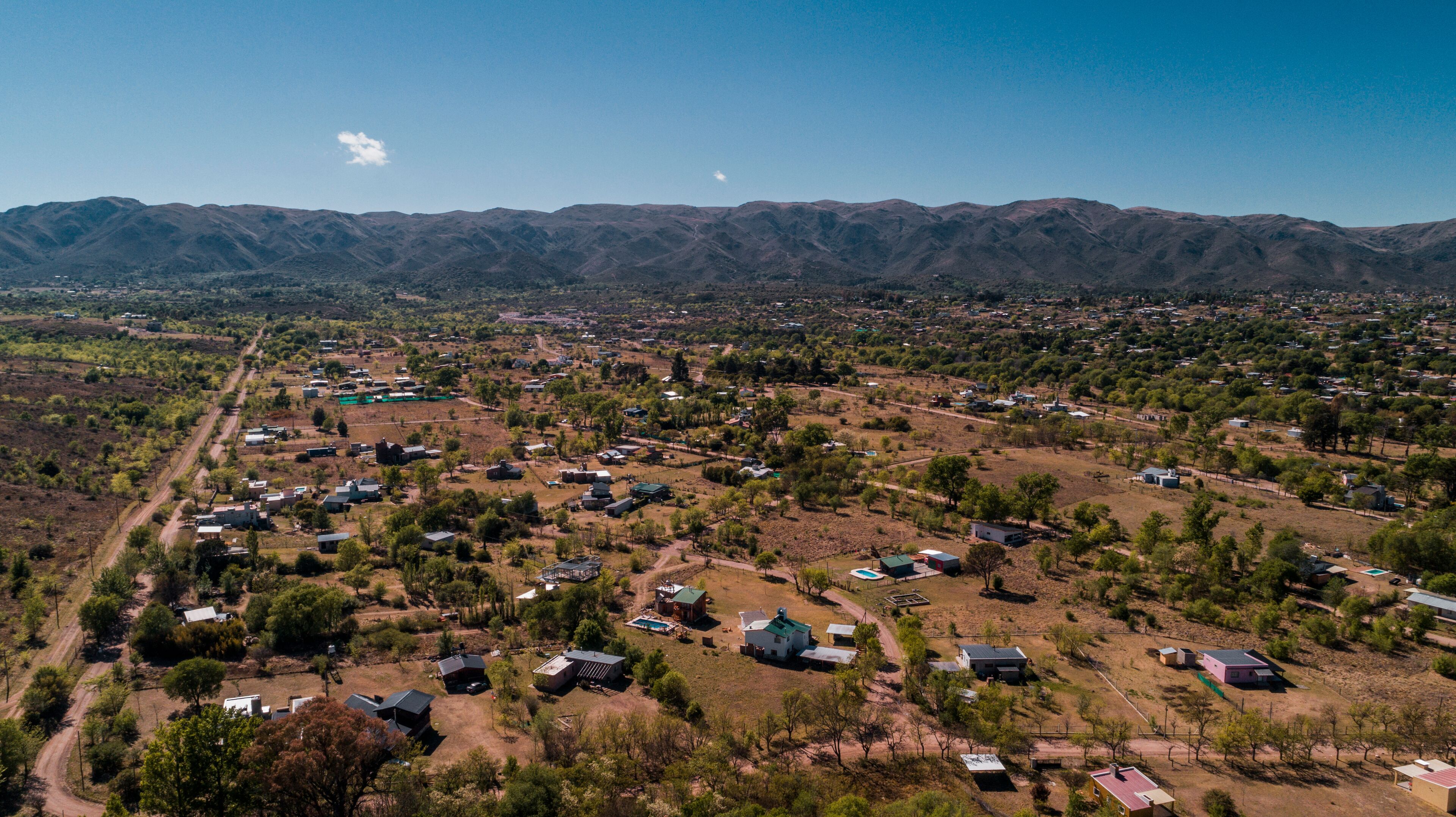 A rural landscape with scattered houses, green vegetation, and mountains in the background.