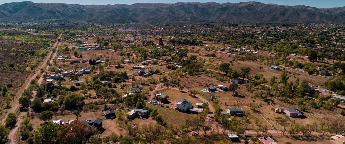 A rural landscape with scattered houses, green vegetation, and mountains in the background.