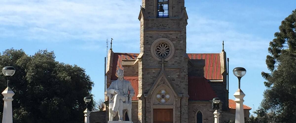 A church with a tall steeple, a clock, and a statue in front.
