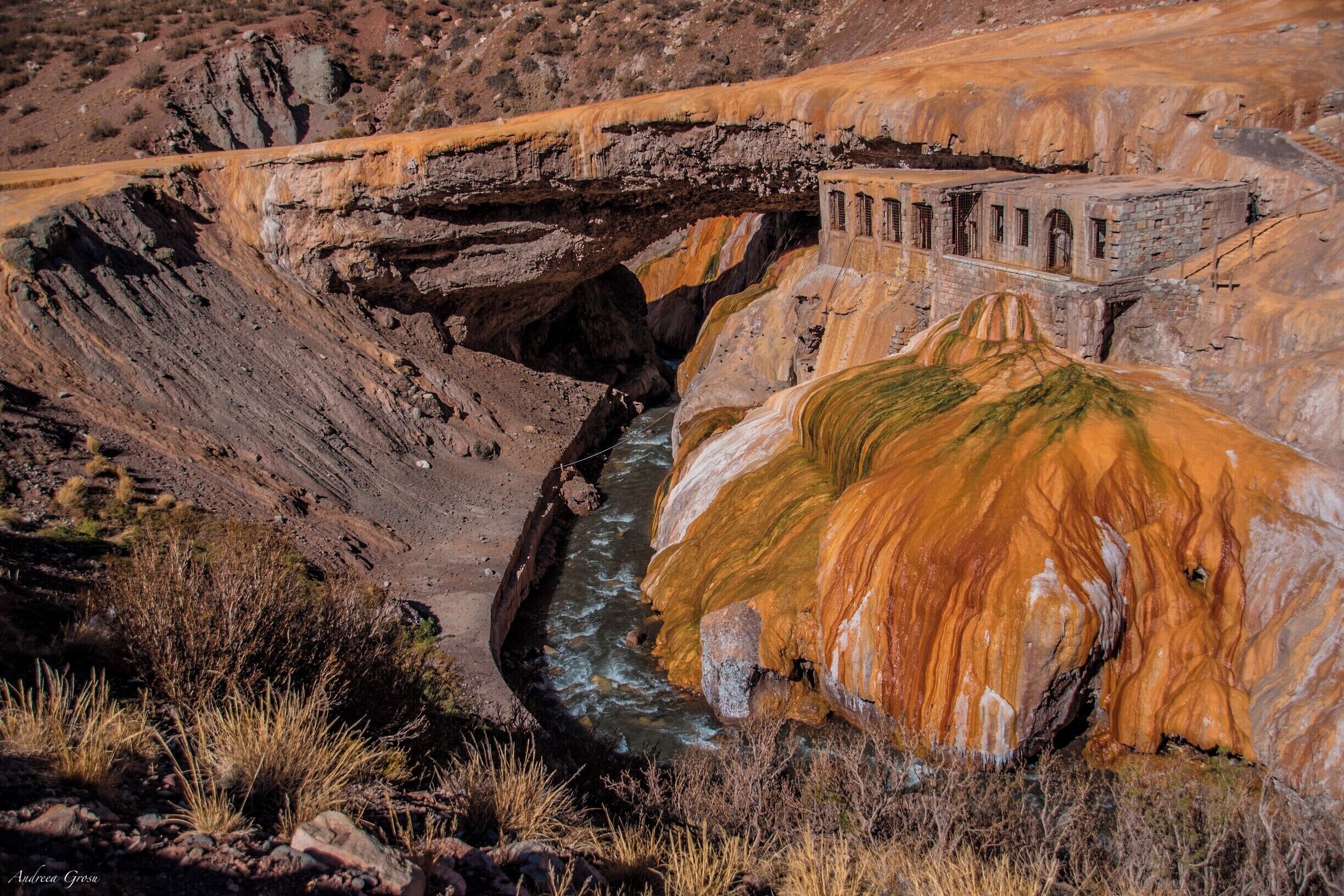 A river flowing through a canyon with a bridge and a large rock formation.