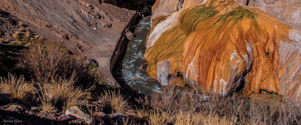 A river flowing through a canyon with a bridge and a large rock formation.