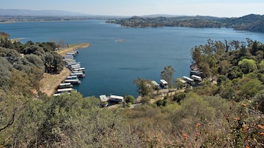 A lake with boats docked along the shore, surrounded by hills and trees.