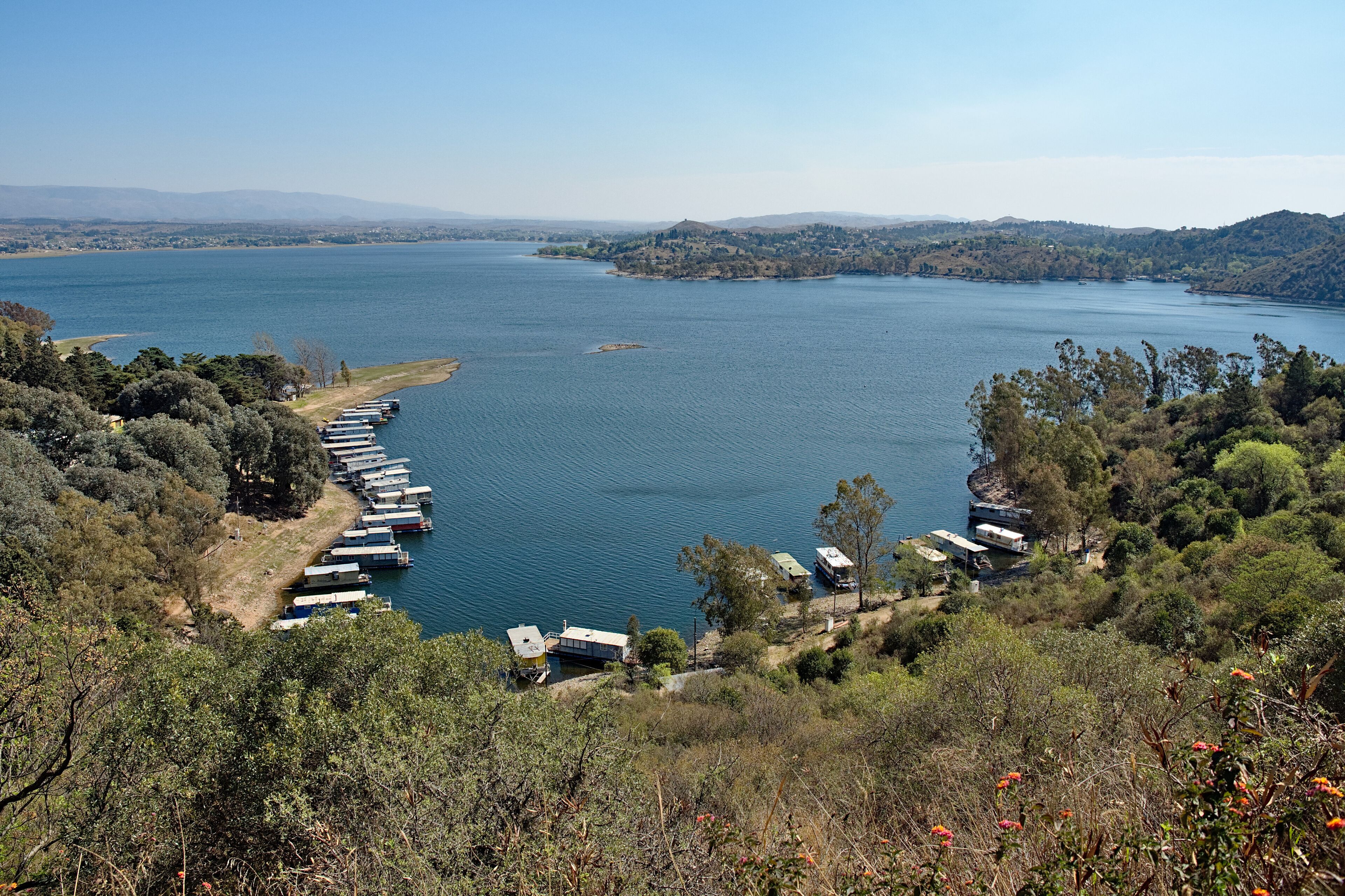 A lake with boats docked along the shore, surrounded by hills and trees.