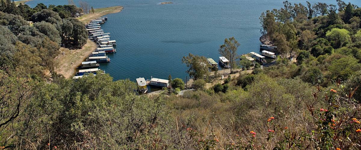 A lake with boats docked along the shore, surrounded by hills and trees.