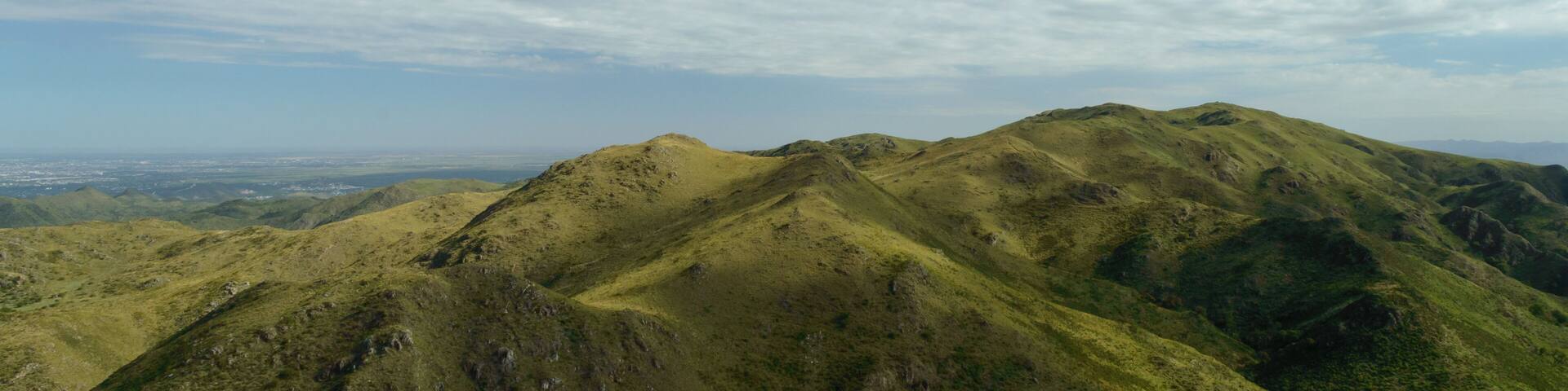 A mountain range with green slopes and a clear sky with scattered clouds.