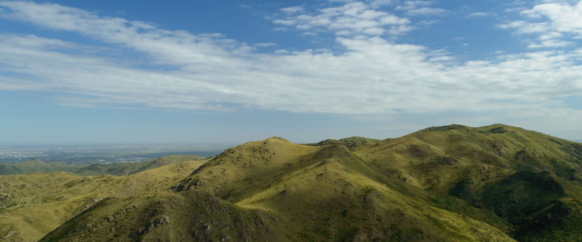 A mountain range with green slopes and a clear sky with scattered clouds.