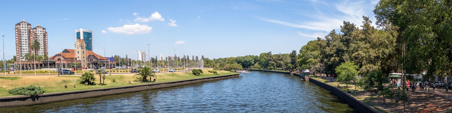 Un río con un puente, un parque con árboles y edificios al fondo.
