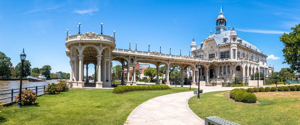 A grand architectural structure with a dome and multiple arches, surrounded by a well-maintained garden and a river.